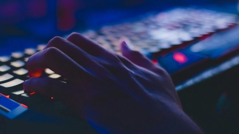 An unidentified person types on a keyboard in a darkened room. (Pexels)