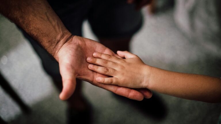 A father is shown holding his child's hand. (Pexels photo)