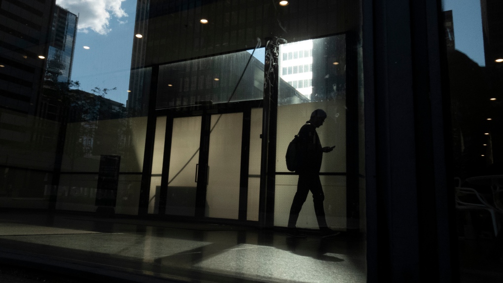 A man walks though a downtown Toronto office building with other buildings reflected in a window in this June 11, 2019 photo. (Graeme Roy / The Canadian Press)