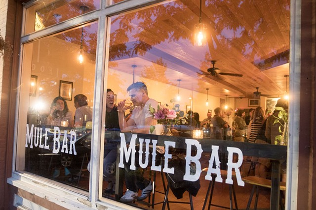 Une fenêtre avec des autocollants en vinyle « Mule Bar » dessus et des personnes en train de dîner visibles à l