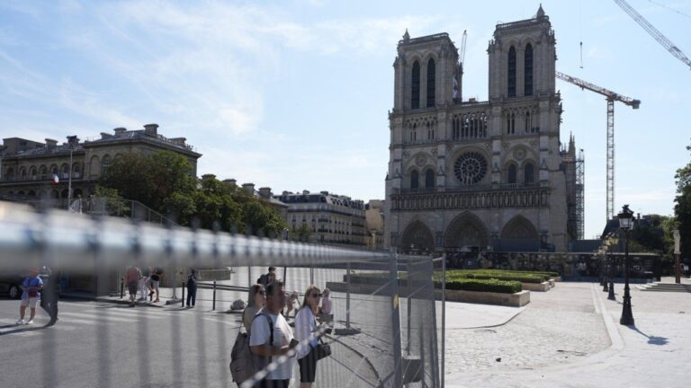 People watch Notre Dame cathedral from outside the security zone set up for the Olympic Games, Thursday, July 18, 2024 in Paris. (AP Photo/David Goldman)