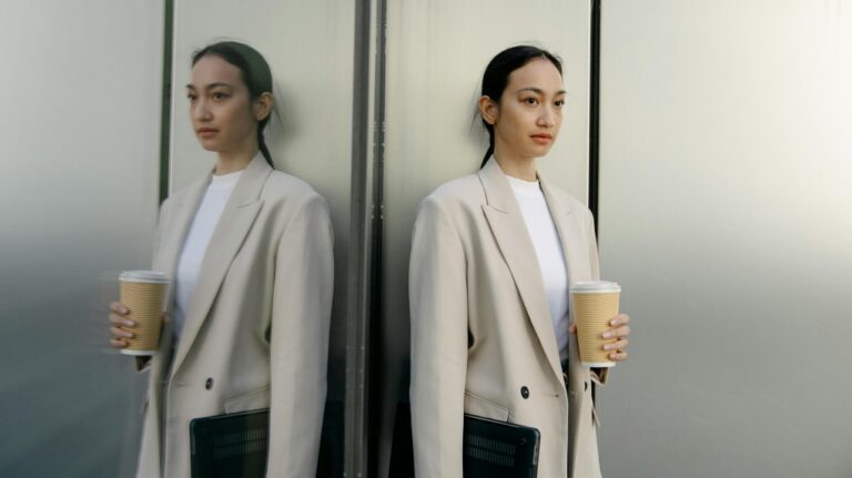In this stock photo, a woman is shown in an office-like setting holding a laptop and a coffee cup. (Pexels)