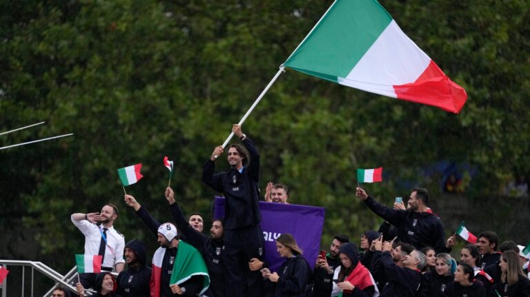 Gianmarco Tamberi waves an Italian flag as the Italian team parades along the Seine river in Paris, France, during the opening ceremony of the 2024 Summer Olympics, Friday, July 26, 2024 (AP Photo/Luca Bruno)