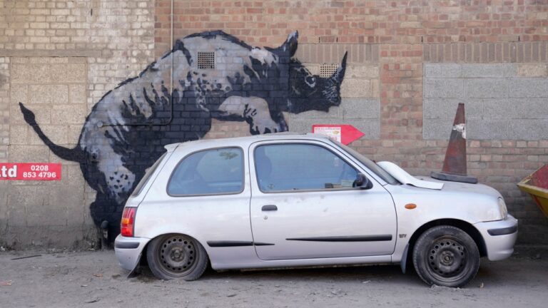A new artwork unveiled by Banksy, depicting a rhinoceros which looks as though it is climbing on top of a car, the eighth artwork in his animal-themed collection, on Westmoor Street in Charlton, south east London, Monday, Aug. 12, 2024. (Lucy North / PA via AP)
