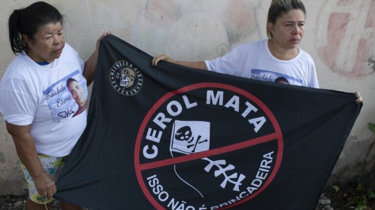 Kelly Christina da Silva, right, whose 23-year-old son died from injuries caused by cuts form a kite line coated in sharp fragments, holds a flag with her mother Maria Enilda da Silva that reads in Portuguese: "The cutting line kills. This is no joke," in Rio de Janeiro, Monday, July 29, 2024. (AP Photo/Bruna Prado)