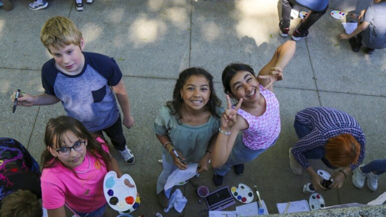 This photo provided by Spokane Public Schools shows Adams Elementary fifth graders pausing to pose for a photo while painting a mural at Spokane Community College, May 2024, in Spokane, Wash. (Spokane Public Schools via AP)