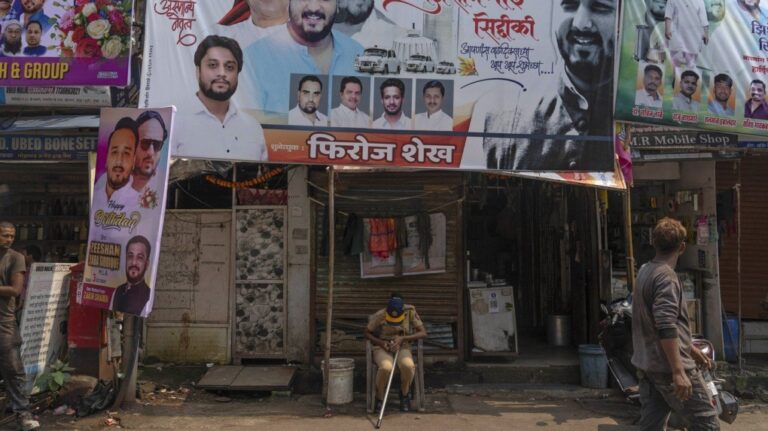 A police person sits below a large hoarding showing a portrait in red turban of Baba Siddique, a senior politician, at the spot where Siddique was shot at outside his son's office in Mumbai and later succumbed to his wounds in a hospital on Saturday night, in Mumbai, India, Sunday, Oct. 13, 2024. (AP Photo/Rafiq Maqbool)