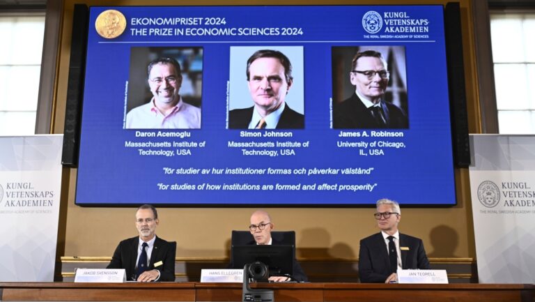 Nobel assembly announces the Nobel memorial prize in economics winners, Daron Acemoglu, Simon Johnson and James A Robinson, seen on screen, at the Royal Swedish Academy of Sciences in Stockholm, Sweden, Monday Oct. 14, 2024. (Christine Olsson/TT News Agency via AP)