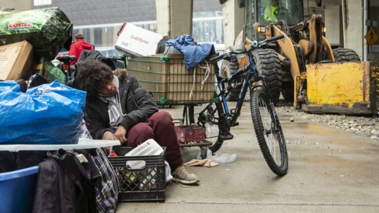 A person who experienced homelessness sits with their belongings as city workers move to clear an encampment on Toronto's Bay Street on May 15, 2020. THE CANADIAN PRESS/Chris Young