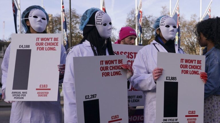 Protesters wearing masks show placards in front of Parliament in London, Friday, Nov. 29, 2024 as British lawmakers started a historic debate on a proposed to help terminally ill adults end their lives in England and Wales.(AP Photo/Alberto Pezzali)