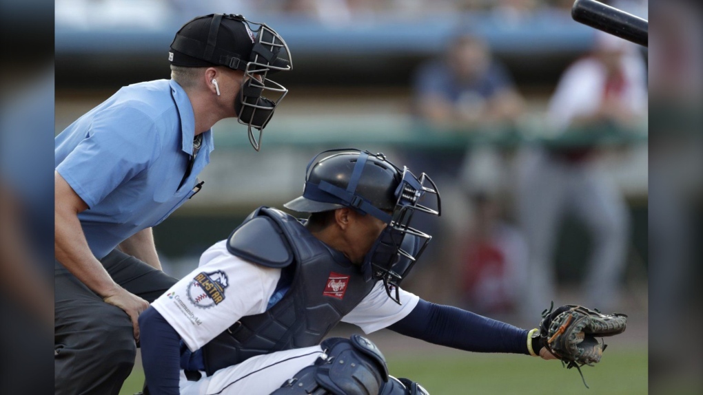 Home plate umpire Brian deBrauwere, left, huddles behind Freedom Division catcher James Skelton, of the York Revolution, as the official wears an earpiece during the first inning of the Atlantic League All-Star minor league baseball game, Wednesday, July 10, 2019, in York, Pa. Major League Baseball will test robot umpires as part of a challenge system during spring training at 13 ballparks hosting 19 teams, which could lead to regular-season use in 2026. (AP Photo/Julio Cortez)