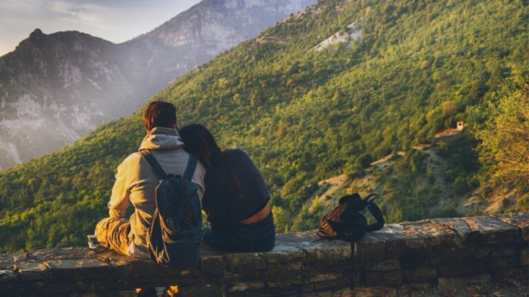 A couple sits while facing a mountain (Pexels)