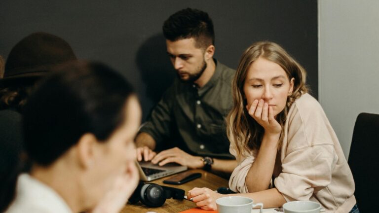 A young woman looks to the side while sitting at a desk with others. (cottonbro studio / Pexels)