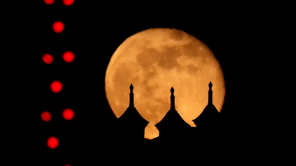 The waning full moon rises beyond buildings in the Country Club Plaza shopping center outlined with Christmas lights, Monday, Dec. 16, 2024, in Kansas City, Mo. (AP Photo/Charlie Riedel)