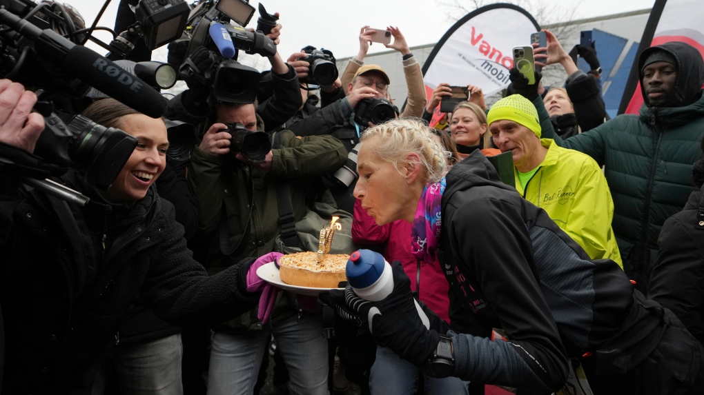 Belgian ultra runner Hilde Dosogne, centre, blows out candles on a cake after crossing the finish line of her 366th consecutive marathon in Ghent, Belgium, Tuesday, Dec. 31, 2024. (AP Photo/Virginia Mayo)